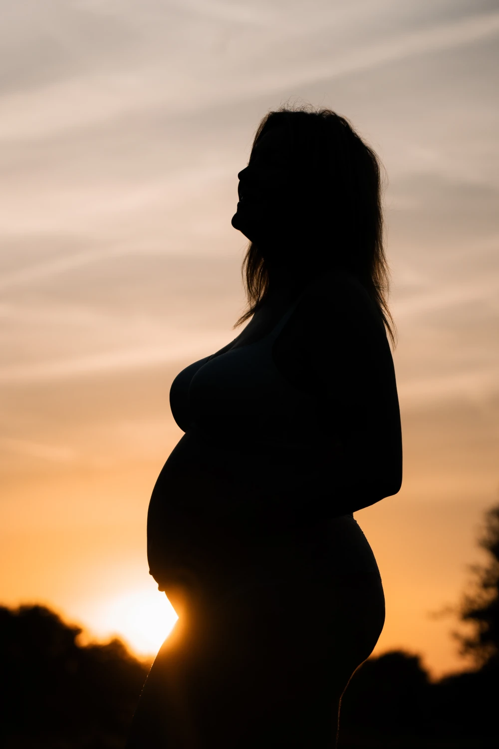 Zwangere vrouw poseert voor de ondergaande zon.
