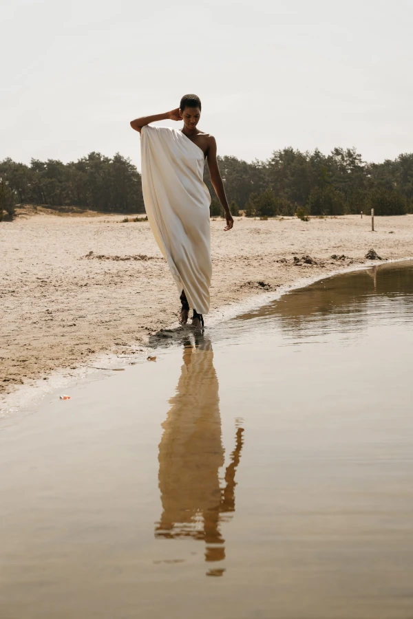 Vrouw poseert naast het water. Ze heeft een wit kleed aan.